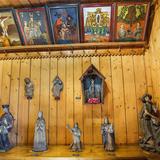 Obrazy na szkle wiszące na drewnianej ścianie, drewniane rzeźby stojące na półce, kapliczki i świątki.