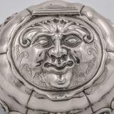 Okrągła dekoracyjna srebrna solniczka, z pokrywką w kształcie twarzy.