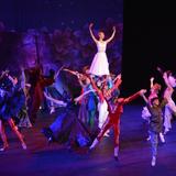 Grupa baletowa unosi balerinę ponad siebie, rzecz dzieje się na scenie w trakcie przedstawienia