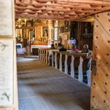 Otwarte drewniane drzwi do wnętrza drewnianego kościoła, po lewej przy drzwiach wiszą dwa obrazki z napisami, za drzwiami widoczny ozdobny niski strop, drewniana podłoga, dalej po prawej drewniane ławki, a w nich kilka osób, na wprost drewniany ołtarz boczny, obrazy i rzeźby na ścianie.
