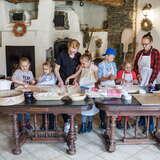 Dzieci pracujące przy stolach z mąką, sitami, dzieżą i innymi przyrządami do przygotowywania pieczywa