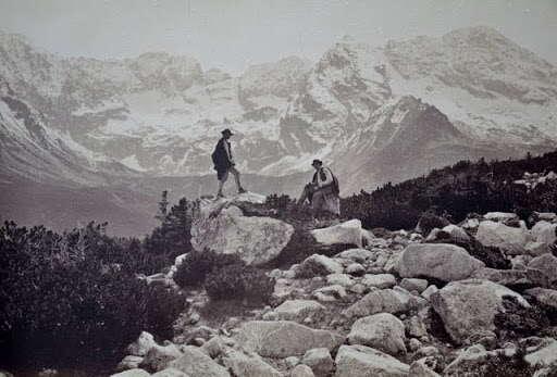 Dwóch górali pozujących w strojach regionalnych na tle tatrzańskiego stawu. Zdjęcie historyczne.
