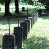 Rząd jednakowych betonowych nagrobków w formie steli z metalowymi krzyżami. W tle drzewa.