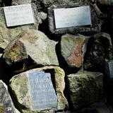 Leżące na sobie kamienie (części nagrobków?) z tablicami nagrobnymi z imionami i nazwiskami zmarłych.